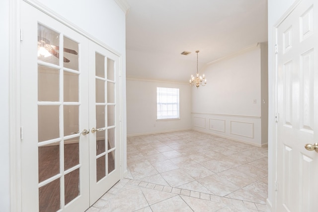 unfurnished room featuring french doors, crown molding, visible vents, a decorative wall, and wainscoting