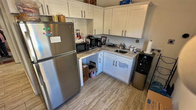 kitchen featuring black microwave, wood finish floors, a sink, white cabinets, and freestanding refrigerator