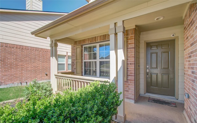 doorway to property featuring covered porch and brick siding