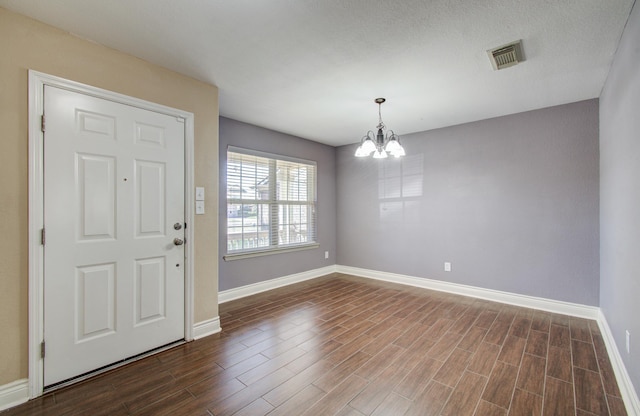 entrance foyer with dark wood-style floors, visible vents, baseboards, and a notable chandelier