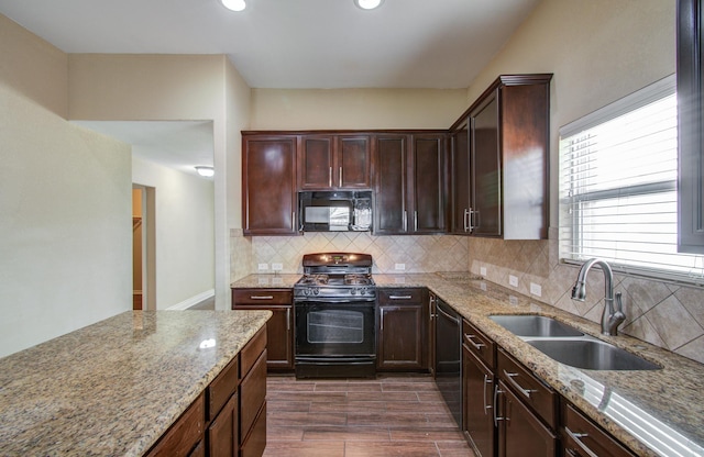 kitchen with dark wood-type flooring, a sink, light stone countertops, black appliances, and backsplash