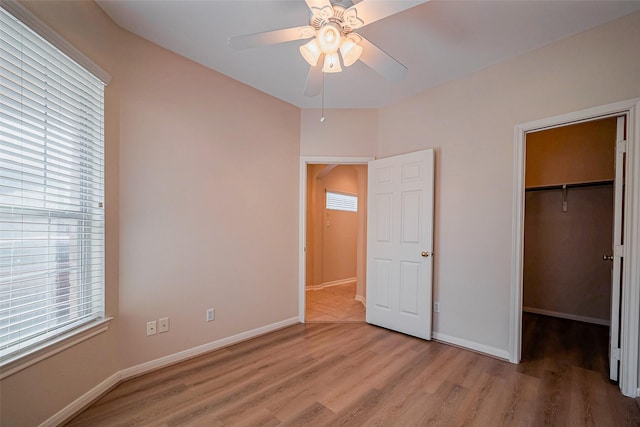 unfurnished bedroom featuring a spacious closet, baseboards, and wood finished floors