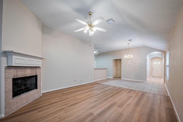 unfurnished living room featuring visible vents, ceiling fan with notable chandelier, light wood-style floors, lofted ceiling, and a tile fireplace