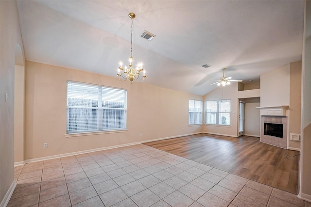 unfurnished living room featuring visible vents, ceiling fan with notable chandelier, light tile patterned floors, lofted ceiling, and a tile fireplace