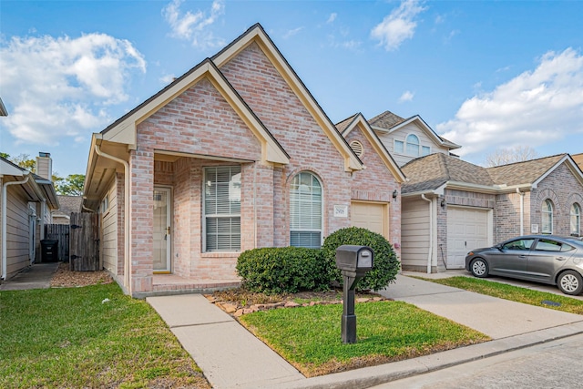 view of front facade with brick siding, a front yard, driveway, an attached garage, and a gate