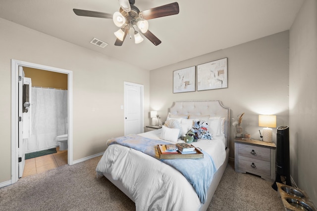 carpeted bedroom with visible vents, ceiling fan, ensuite bath, baseboards, and tile patterned floors