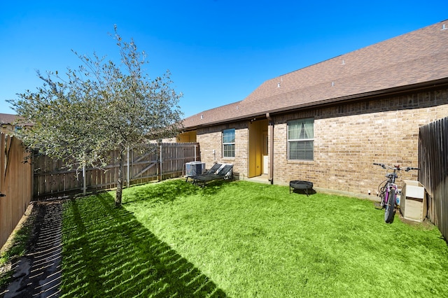 back of property featuring roof with shingles, a yard, brick siding, central air condition unit, and a fenced backyard