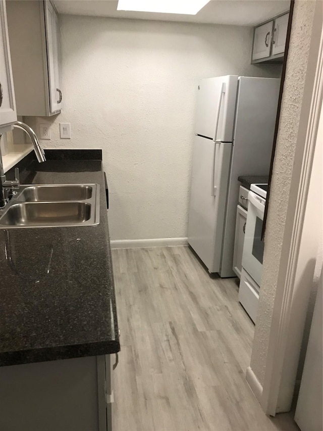 kitchen with white appliances, dark countertops, a sink, and light wood-style flooring