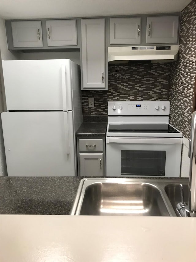 kitchen featuring white appliances, tasteful backsplash, dark countertops, gray cabinets, and under cabinet range hood