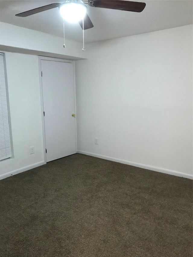 empty room featuring dark colored carpet, a ceiling fan, and baseboards