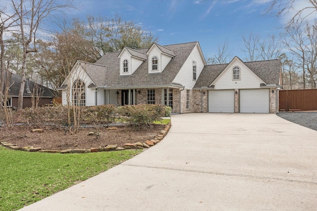 cape cod-style house featuring roof with shingles, concrete driveway, fence, brick siding, and a garage