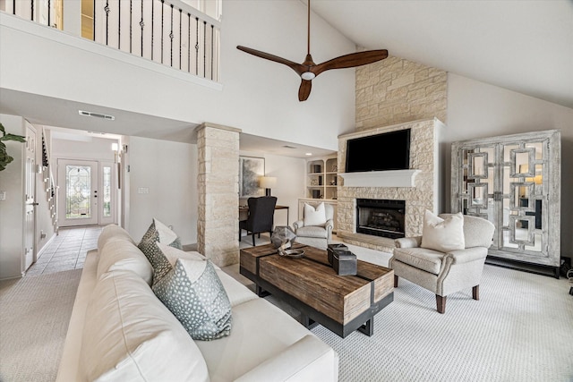 carpeted living area with visible vents, ceiling fan, a stone fireplace, tile patterned floors, and ornate columns