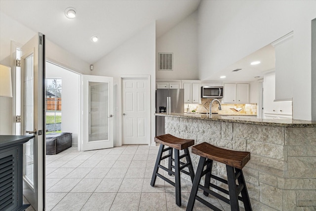 kitchen with light stone countertops, decorative backsplash, appliances with stainless steel finishes, white cabinetry, and a sink