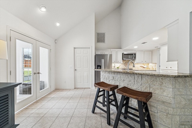 kitchen featuring stainless steel appliances, french doors, a sink, white cabinetry, and high vaulted ceiling