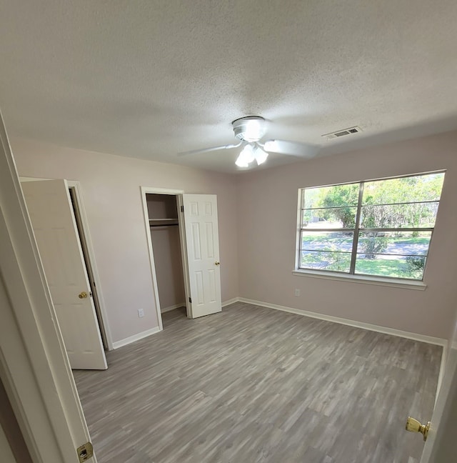 unfurnished bedroom with a textured ceiling, wood finished floors, visible vents, baseboards, and a closet