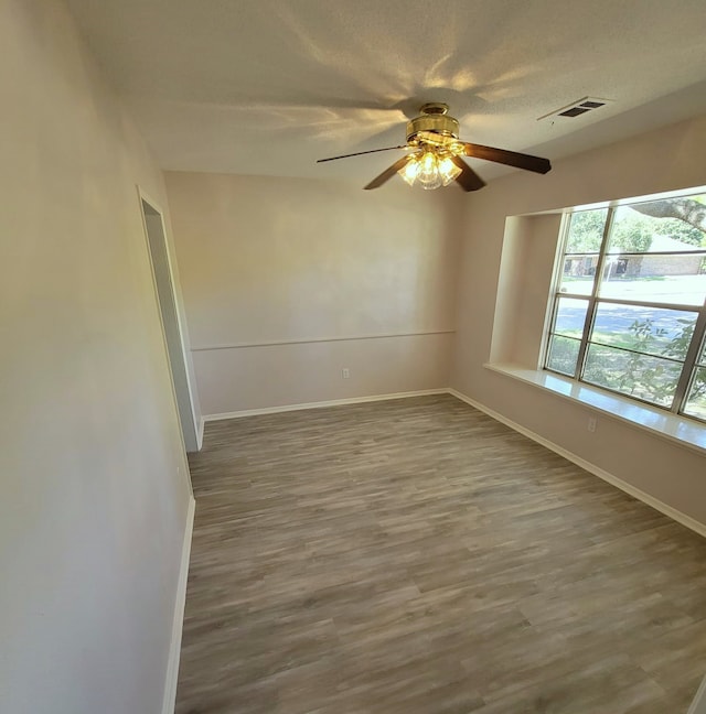 spare room with a ceiling fan, visible vents, baseboards, and wood finished floors