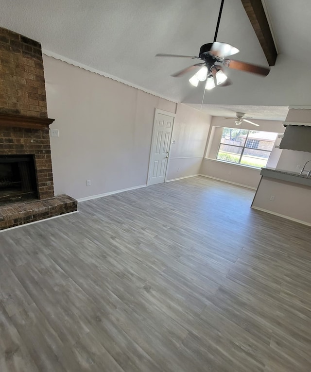 unfurnished living room with vaulted ceiling with beams, a fireplace, baseboards, and wood finished floors