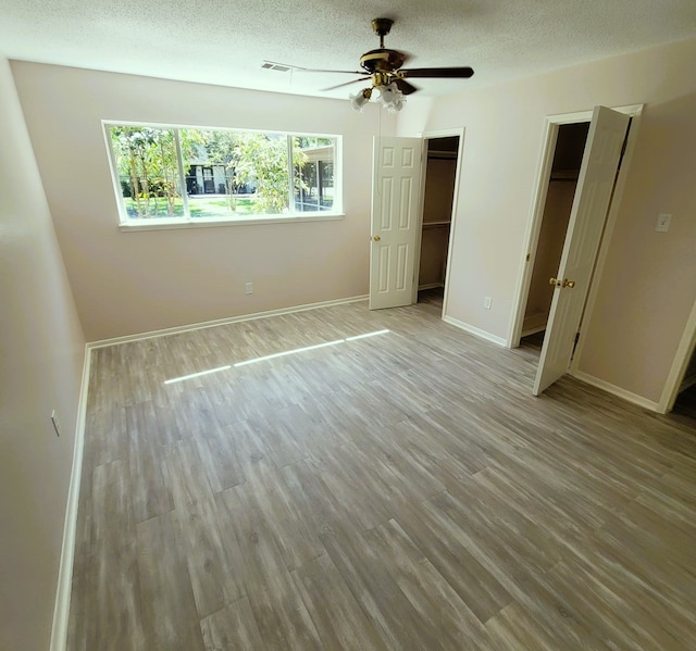 unfurnished bedroom with ceiling fan, a textured ceiling, baseboards, and wood finished floors