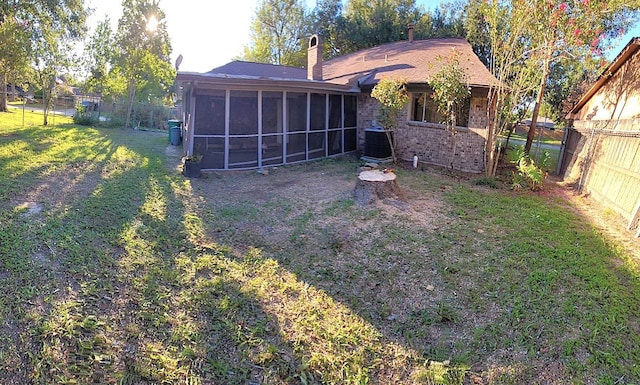 rear view of house with a sunroom, a fenced backyard, a chimney, a yard, and brick siding