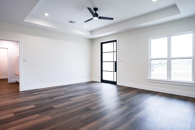 spare room with a tray ceiling, dark wood-style flooring, and baseboards