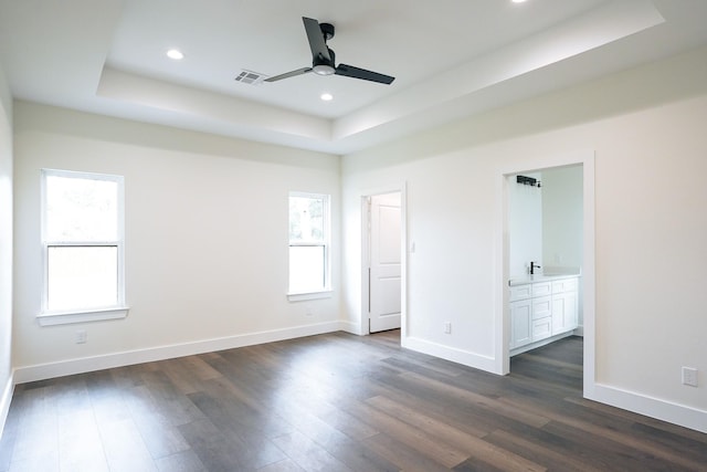 unfurnished bedroom featuring baseboards, visible vents, dark wood-style flooring, and a tray ceiling