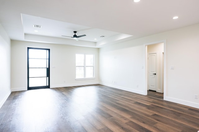 spare room with visible vents, dark wood finished floors, baseboards, a tray ceiling, and recessed lighting