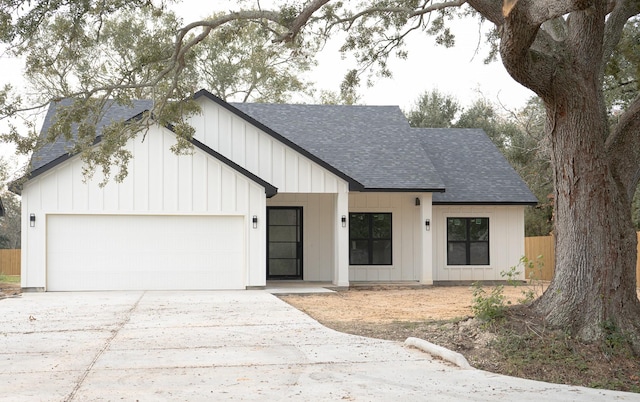 modern farmhouse featuring a shingled roof, concrete driveway, an attached garage, fence, and board and batten siding