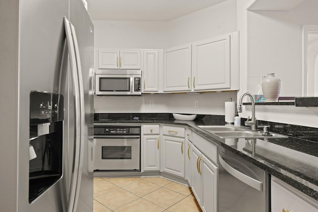 kitchen with appliances with stainless steel finishes, white cabinetry, a sink, light tile patterned flooring, and dark stone counters