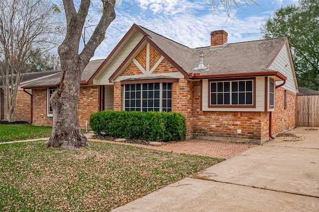 view of front facade featuring roof with shingles, brick siding, a chimney, and fence