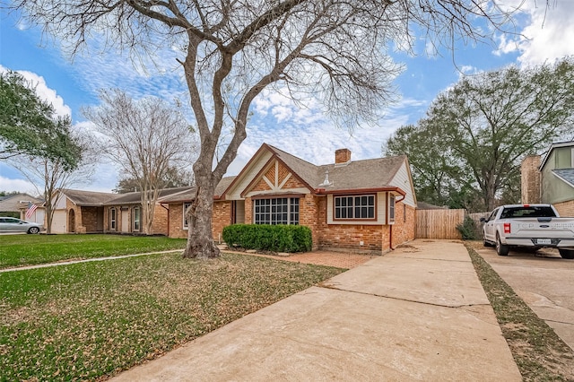 view of front of home with brick siding, fence, concrete driveway, a front lawn, and a chimney