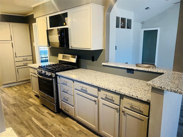 kitchen with arched walkways, light wood-style flooring, light stone counters, stainless steel gas range, and black microwave