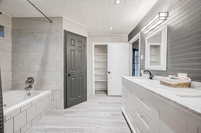 full bath featuring double vanity, tiled shower / bath combo, a sink, and wood finished floors