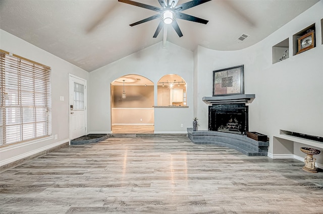 living area featuring arched walkways, a fireplace, visible vents, vaulted ceiling, and wood finished floors