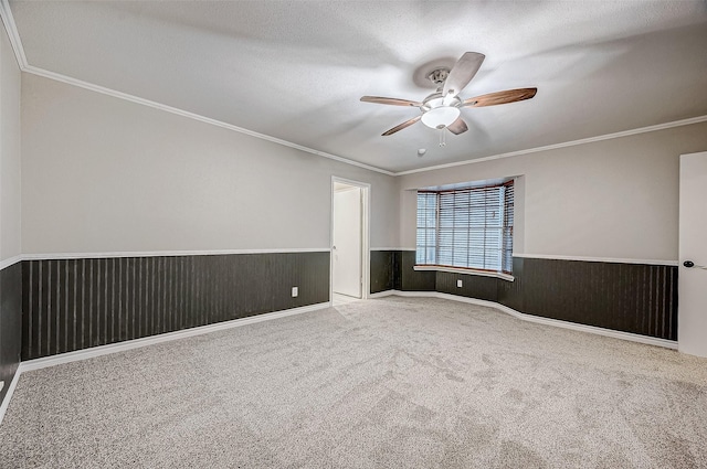 carpeted empty room with crown molding, wainscoting, ceiling fan, wooden walls, and a textured ceiling