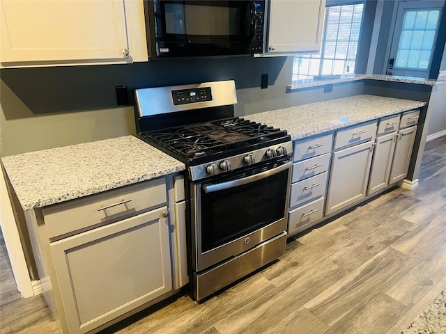 kitchen featuring light wood-style flooring, light stone counters, stainless steel gas range, gray cabinetry, and black microwave