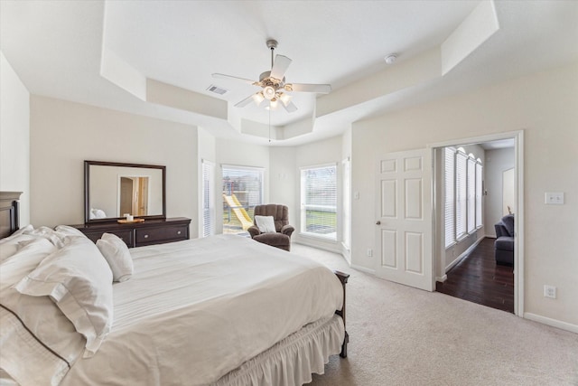 bedroom featuring visible vents, baseboards, ceiling fan, a tray ceiling, and carpet floors