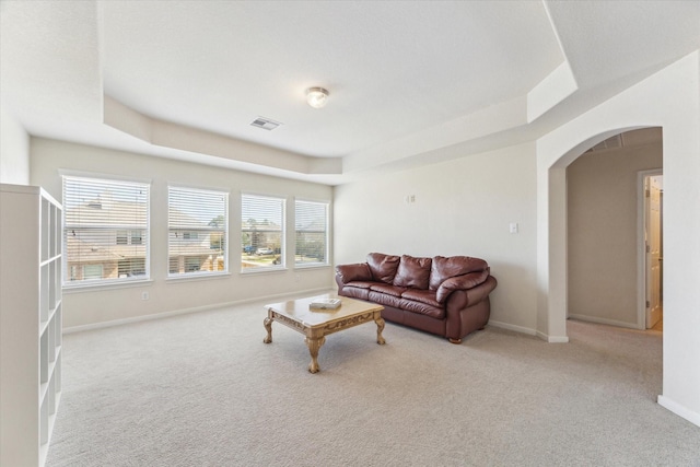 carpeted living area with visible vents, arched walkways, a raised ceiling, and baseboards