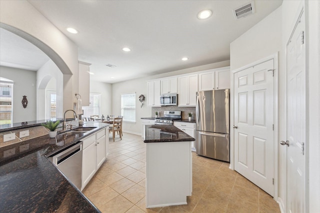 kitchen with light tile patterned floors, a sink, appliances with stainless steel finishes, backsplash, and a center island