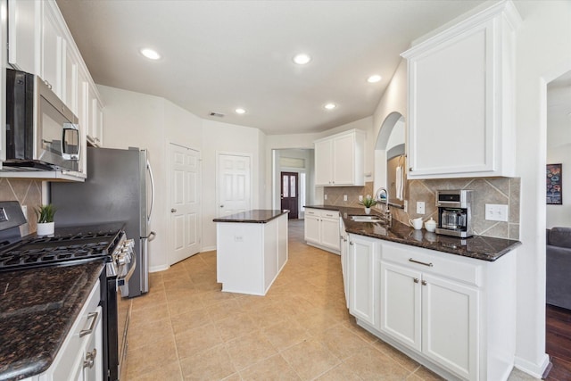 kitchen featuring arched walkways, a kitchen island, a sink, white cabinetry, and appliances with stainless steel finishes