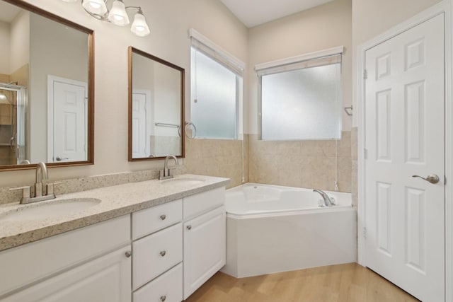 bathroom featuring wood finished floors, a garden tub, a sink, and double vanity