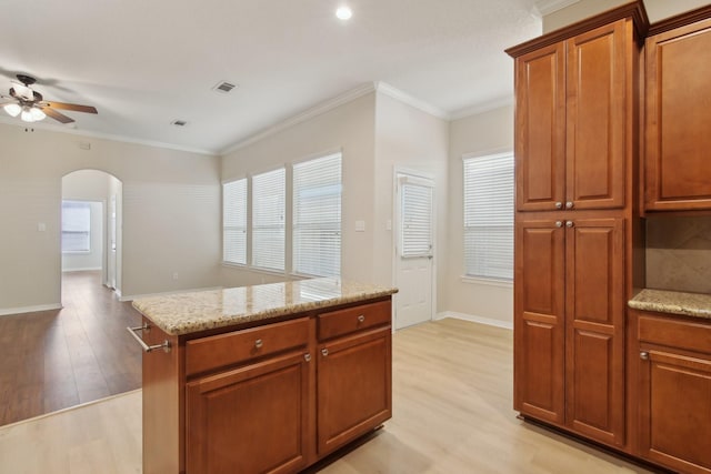 kitchen with arched walkways, light stone counters, a ceiling fan, light wood-style floors, and ornamental molding