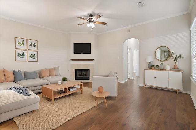 living area featuring arched walkways, a fireplace, visible vents, ornamental molding, and wood finished floors