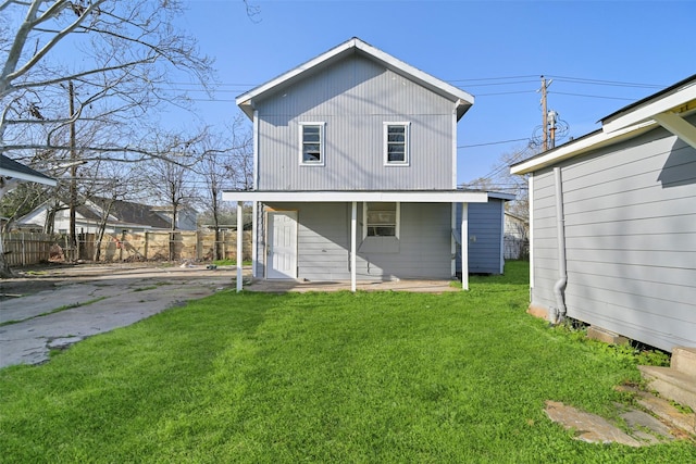 rear view of house with covered porch, fence, and a yard