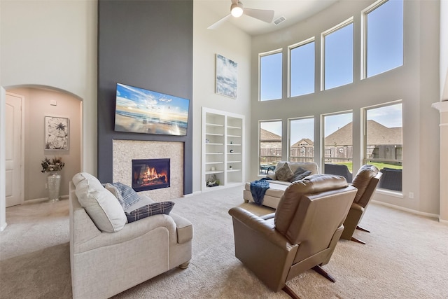 carpeted living room with visible vents, arched walkways, baseboards, a glass covered fireplace, and ceiling fan