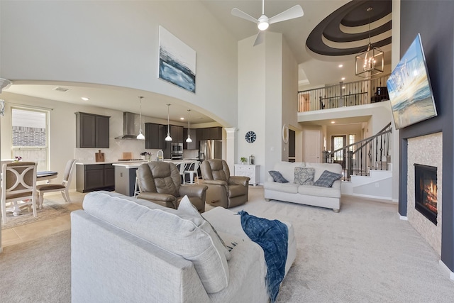 living room featuring light carpet, a high ceiling, arched walkways, and a glass covered fireplace