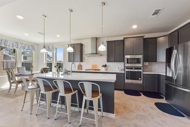 kitchen featuring stainless steel appliances, light countertops, visible vents, a kitchen island with sink, and wall chimney exhaust hood