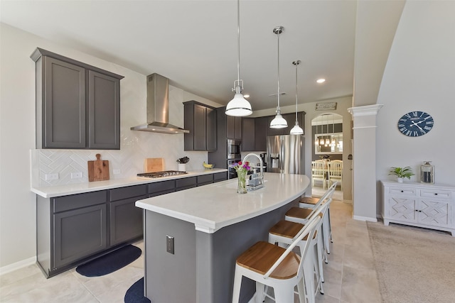 kitchen featuring stainless steel appliances, light countertops, decorative backsplash, an island with sink, and wall chimney exhaust hood