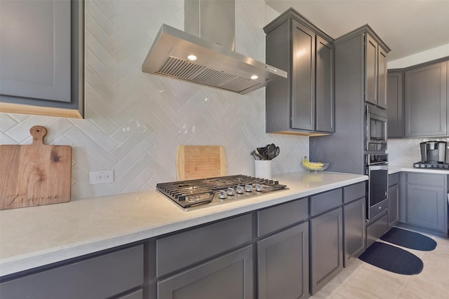 kitchen with stainless steel appliances, light countertops, wall chimney range hood, and light tile patterned floors