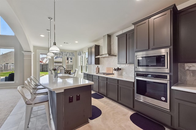 kitchen featuring tasteful backsplash, light countertops, appliances with stainless steel finishes, a sink, and wall chimney exhaust hood