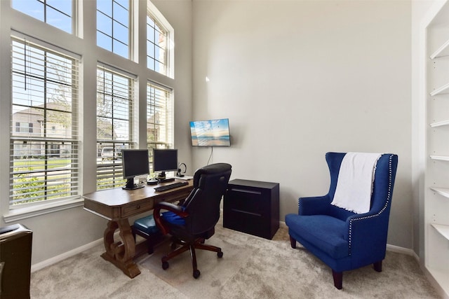 carpeted home office with a healthy amount of sunlight, a towering ceiling, and baseboards